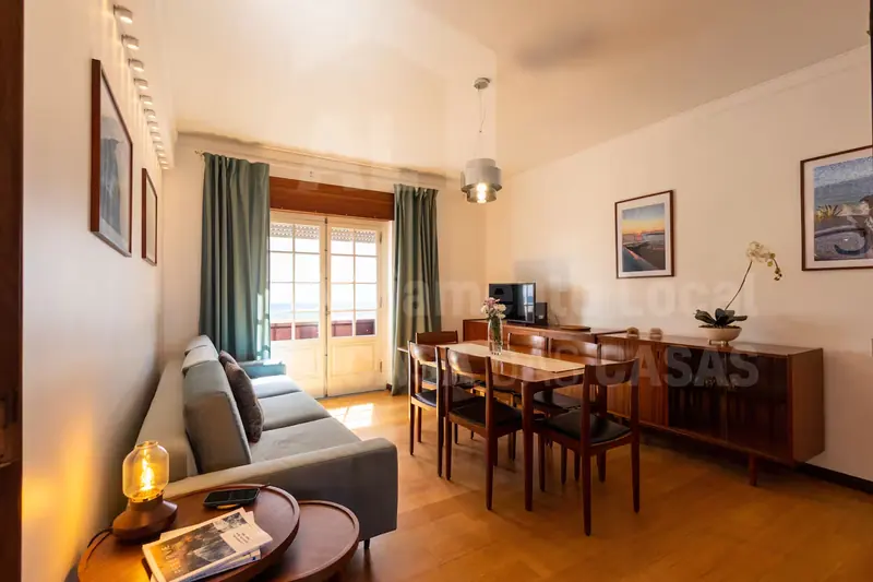Zona de estar com sofá, candeeiro de mesa e aparador com orquídea