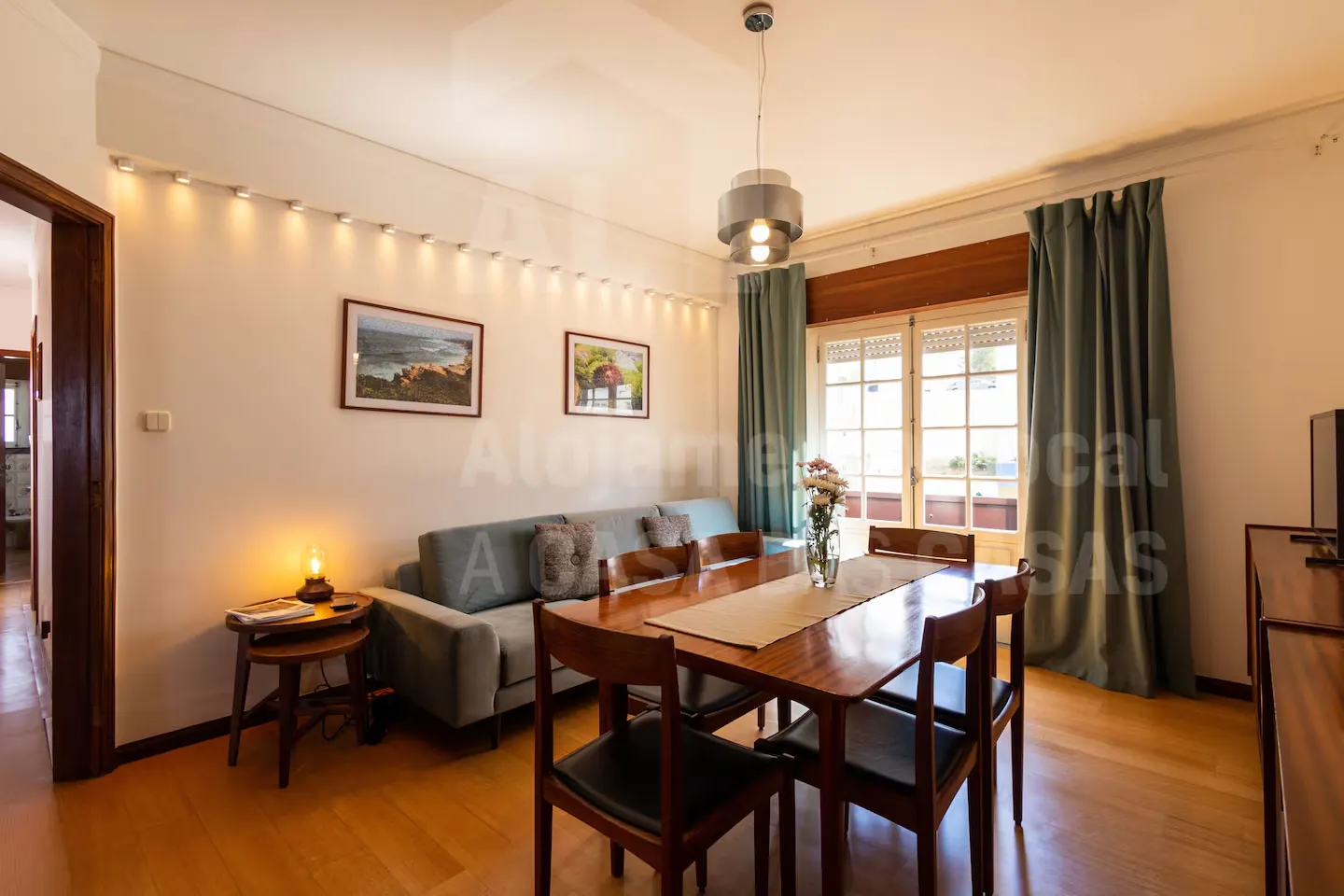 Sala com mesa de jantar em madeira, sofá azul e cortinas verdes junto às janelas