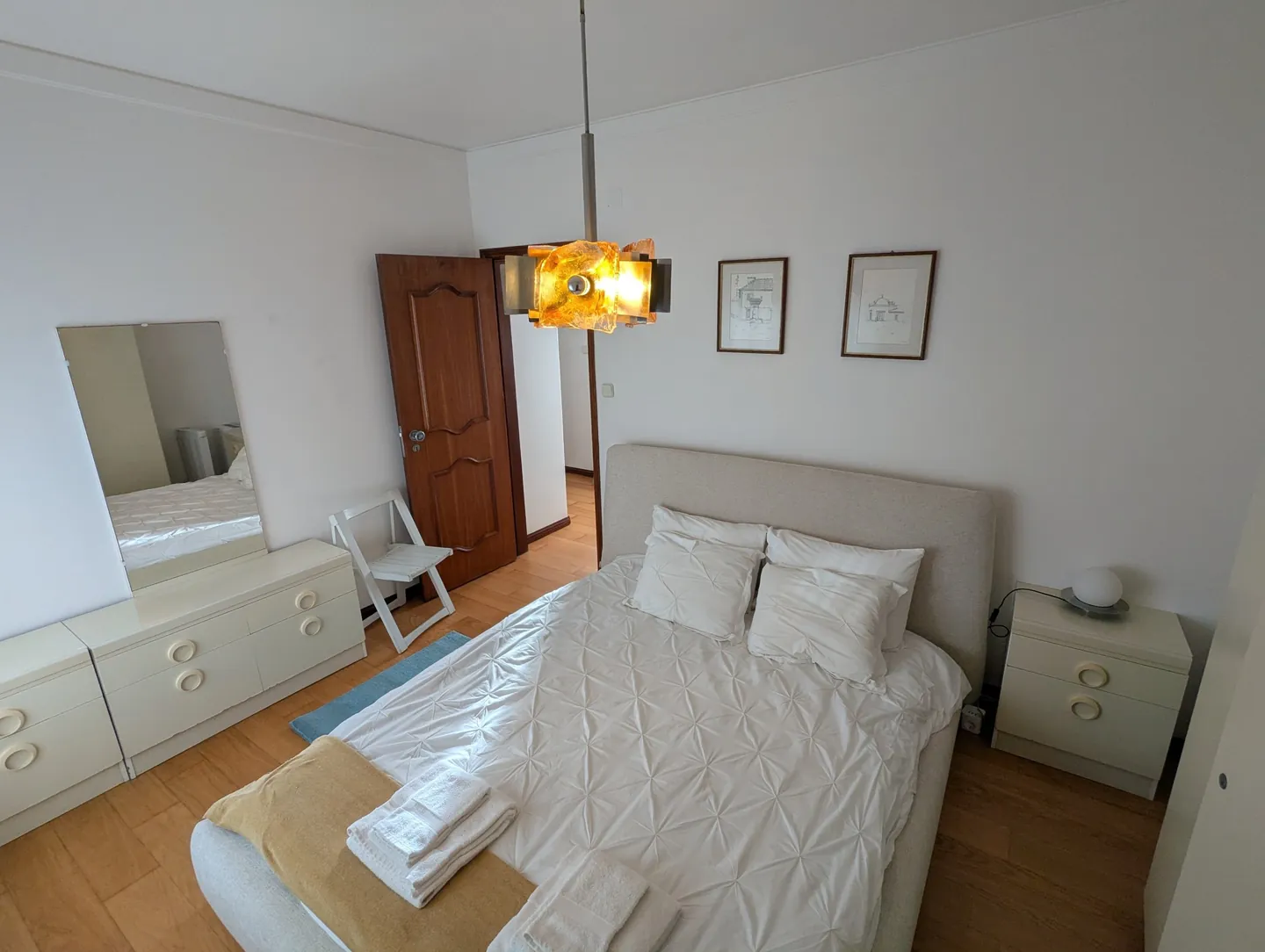 Quarto de casal com cama de casal, cómoda com espelho e mesas de cabeceira