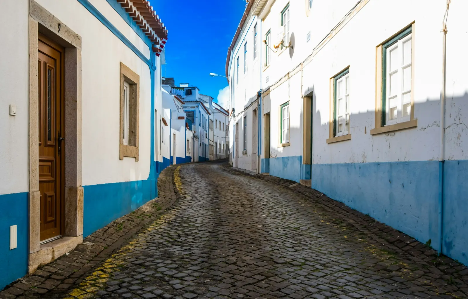 Rua empedrada da Ericeira com casas brancas de barras azuis