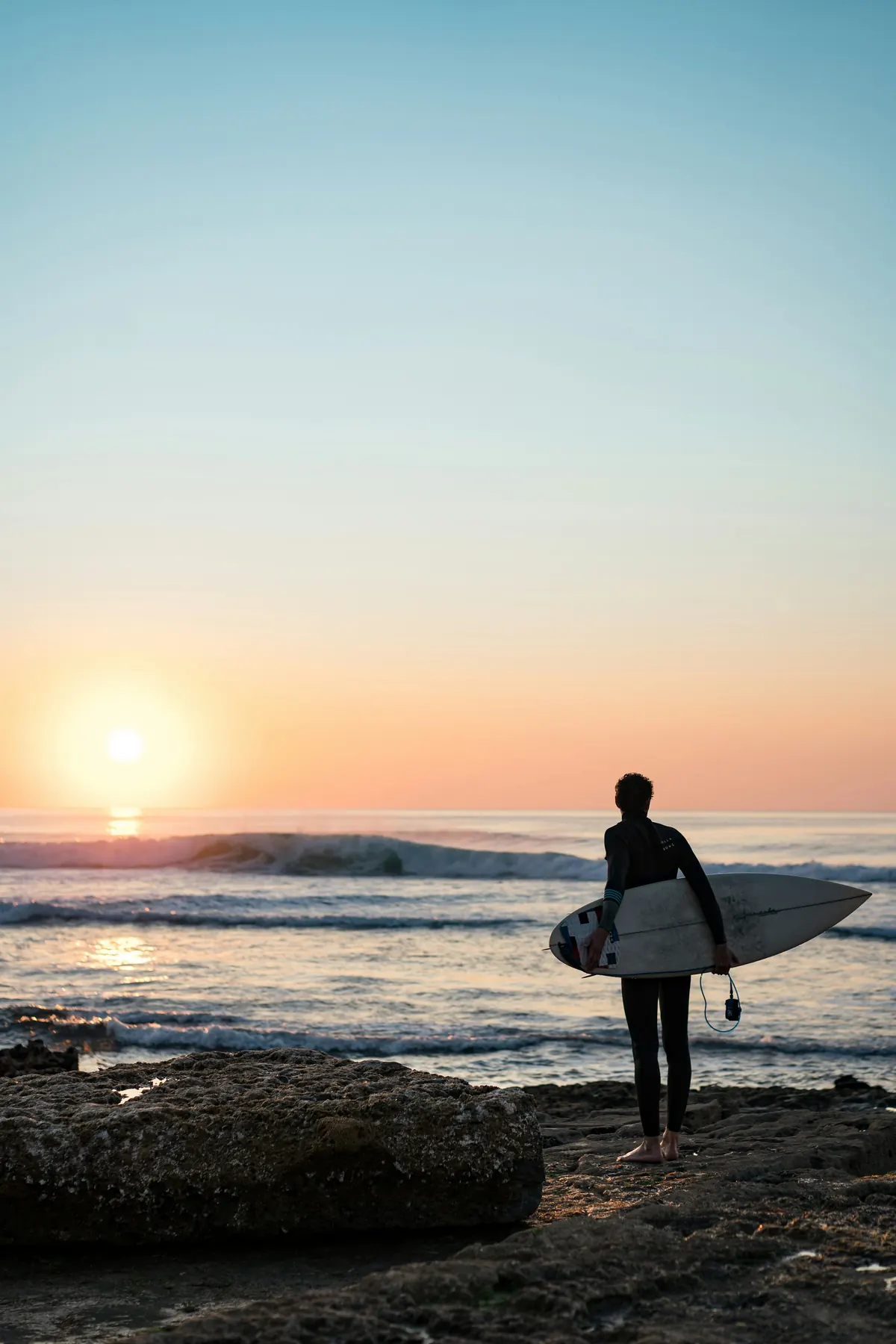 Surfista com prancha sobre as rochas ao pôr do sol